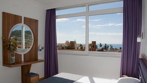 A hotel room with a large window, a bed, a bedside table, and a mirror. - Sealine Hotel (Alanya)