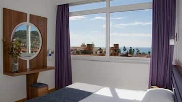 Ein Hotelzimmer mit großem Fenster, einem Bett, einem Nachttisch und einem Spiegel.