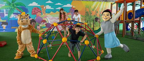A play area with a colorful mural, a play structure, and a mascot.