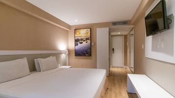 Quarto de hotel moderno com uma cama grande, televisão de tela plana na parede e um quadro sobre a cama.
