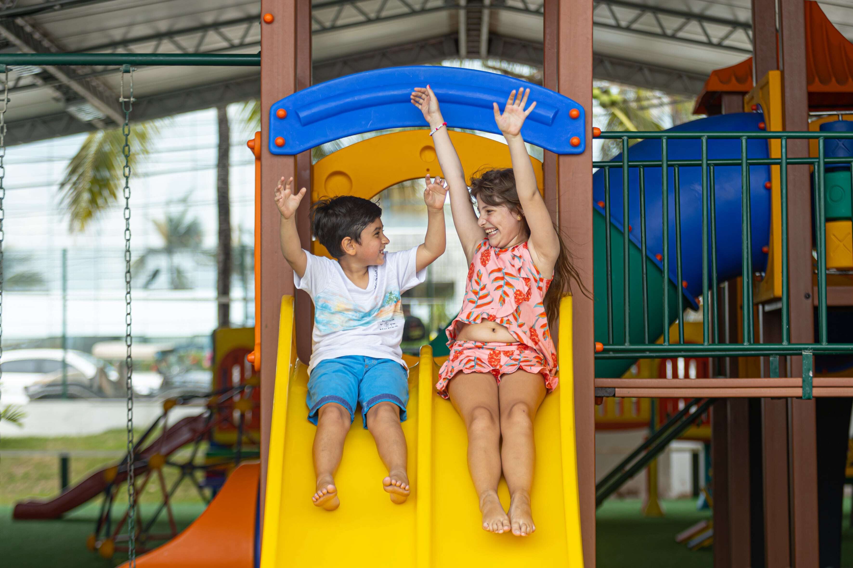 Two children on a yellow slide at a playground.