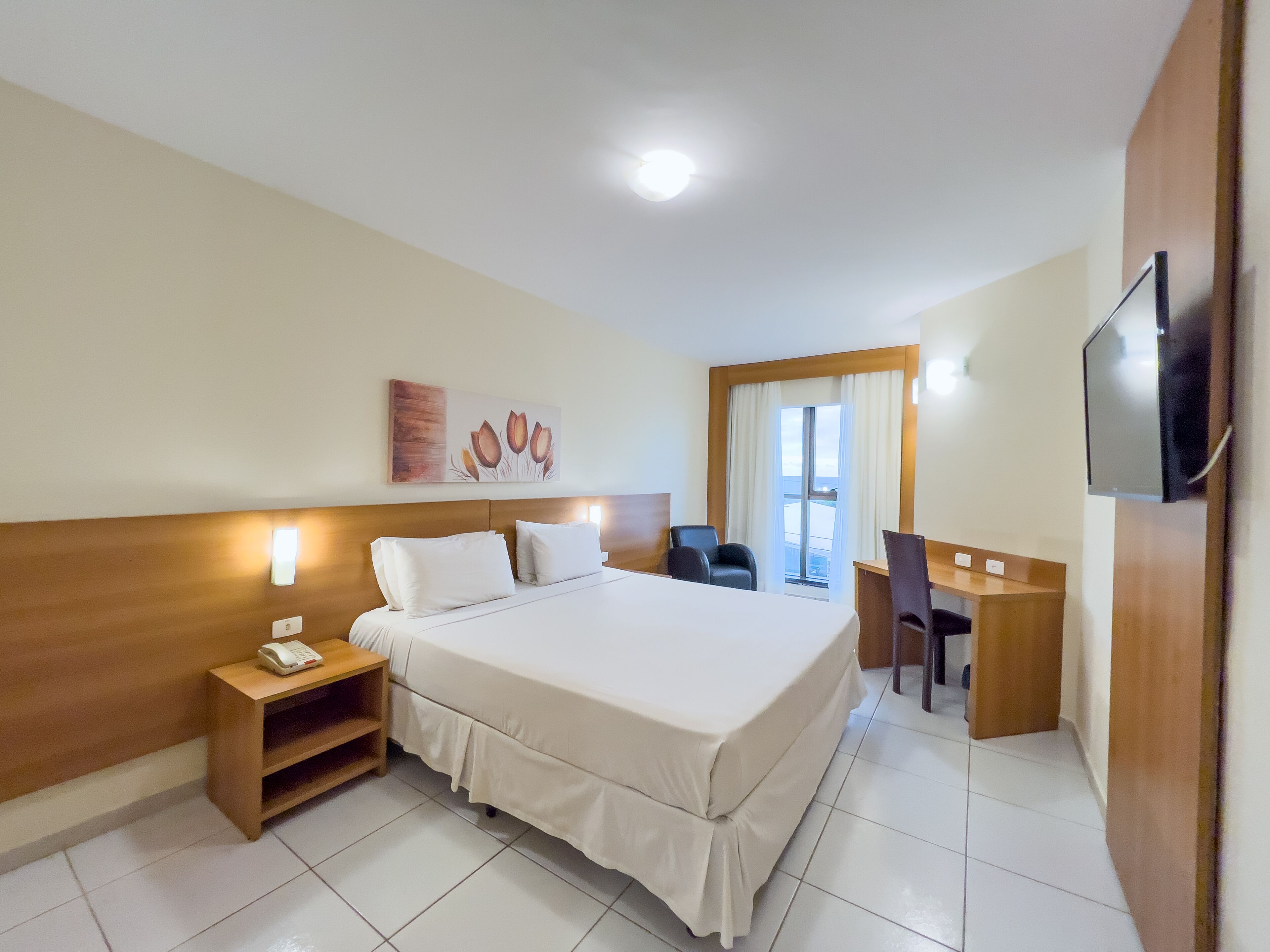 A hotel room with a bed, bedside table, desk, chair, and a television.