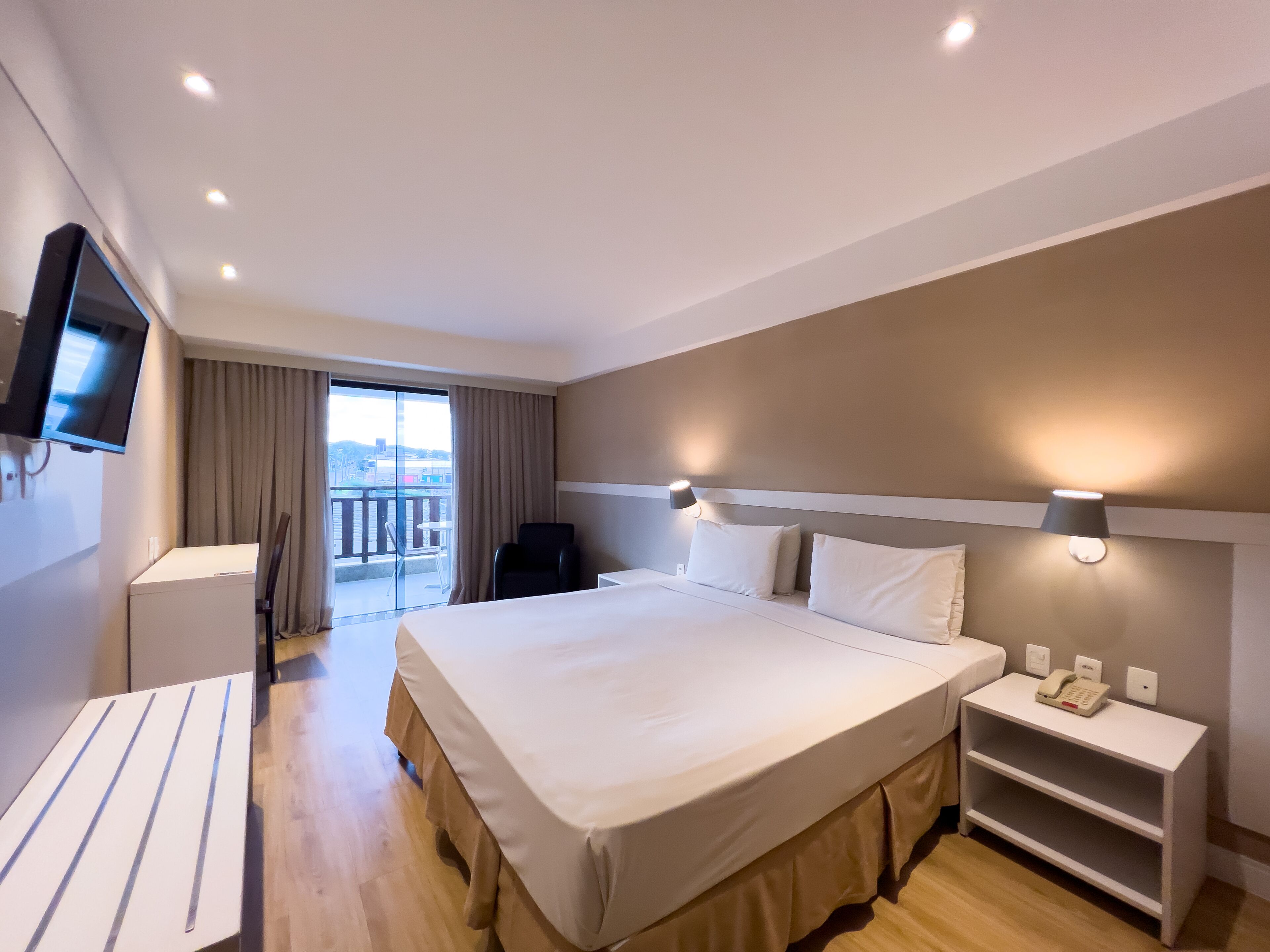 Une chambre d’hôtel avec un grand lit, des tables de chevet, une télévision et un balcon avec des rideaux.