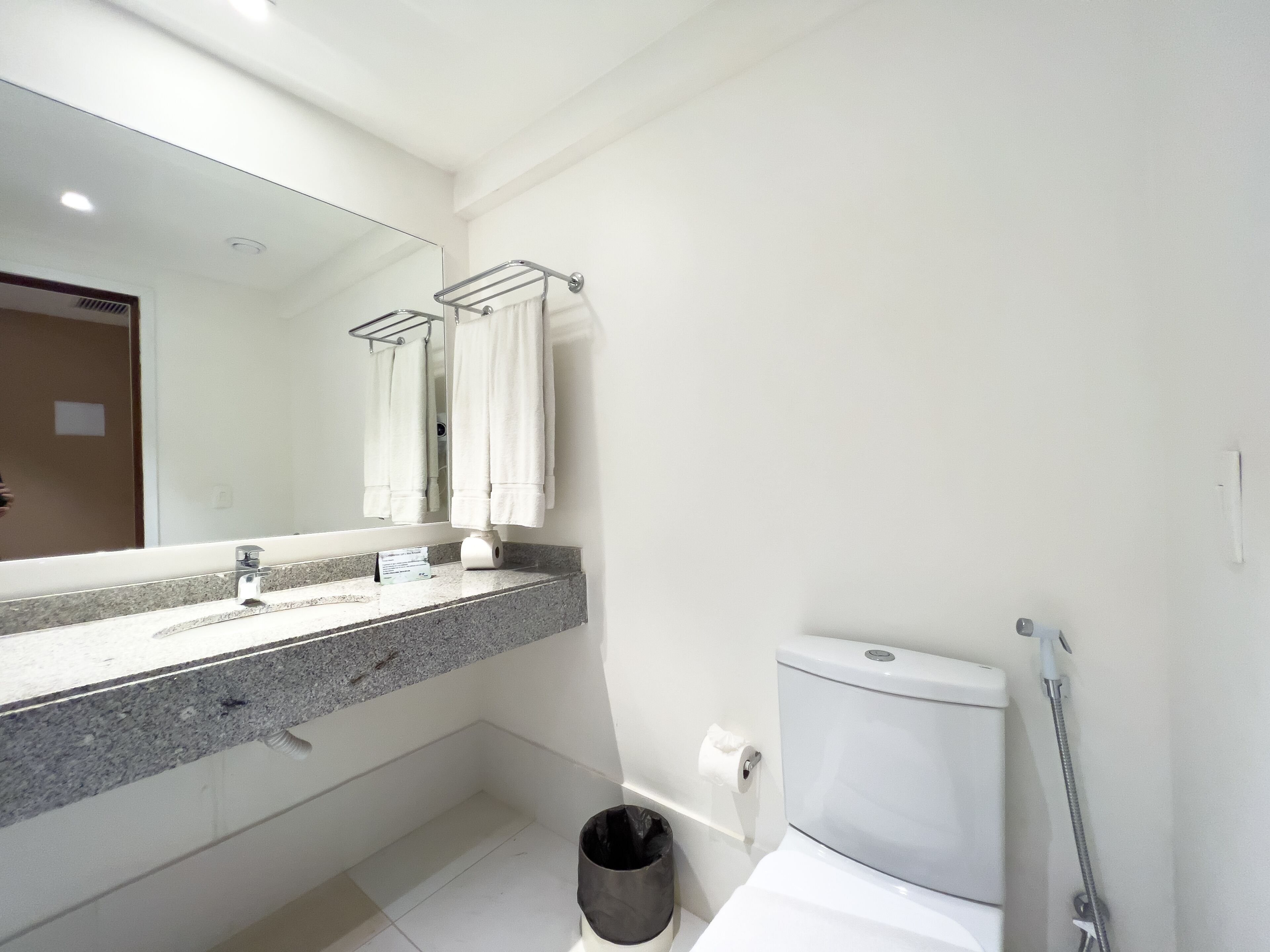 A modern bathroom with a granite countertop, a toilet, a bidet, and a towel rack.