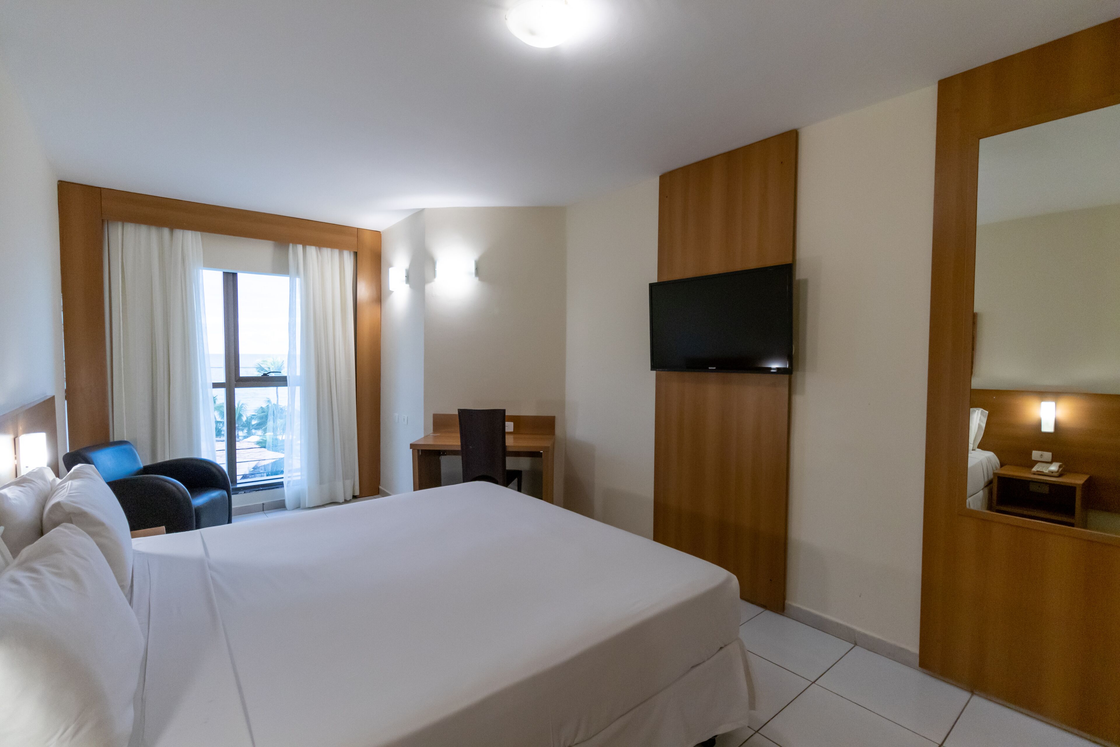 A hotel room with a large bed, a desk, a chair, a television, and a window with curtains.