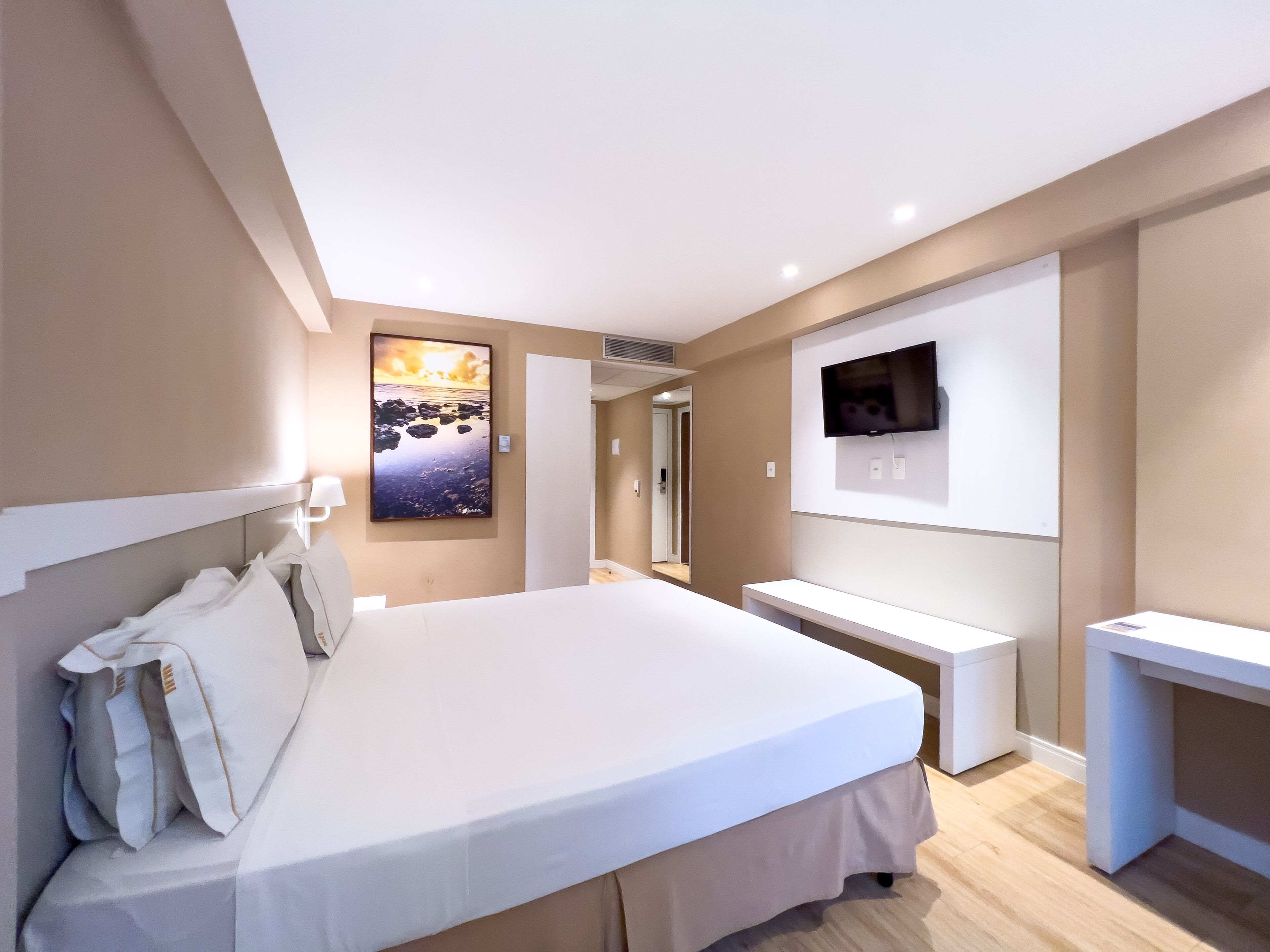 Habitación de hotel moderna con una cama grande, un televisor de pantalla plana montado en la pared y un escritorio pequeño.