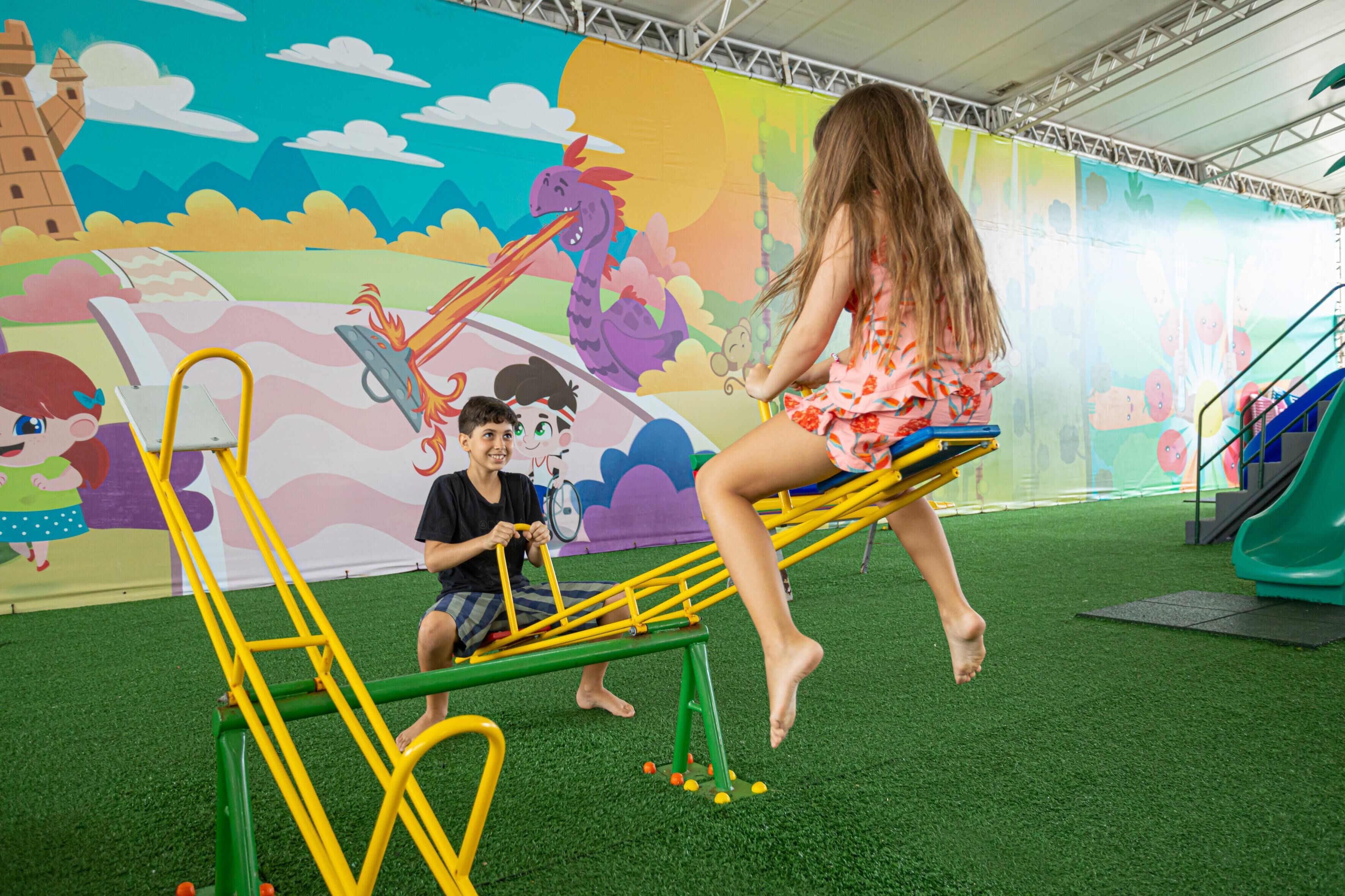 A child and an adult on a seesaw with a colorful mural in the background.