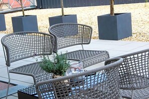 A wicker outdoor seating area with a table and chairs, surrounded by planters and a small decorative item. - Schlossberghotel (Greiz)