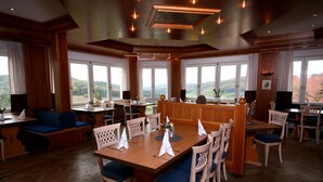 Un comedor amplio con mobiliario de madera, grandes ventanales que ofrecen vistas al campo y un techo alto con iluminación empotrada.
