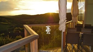 Un balcón con sillas de mimbre y una mesa, con vistas a un paisaje pintoresco al atardecer.