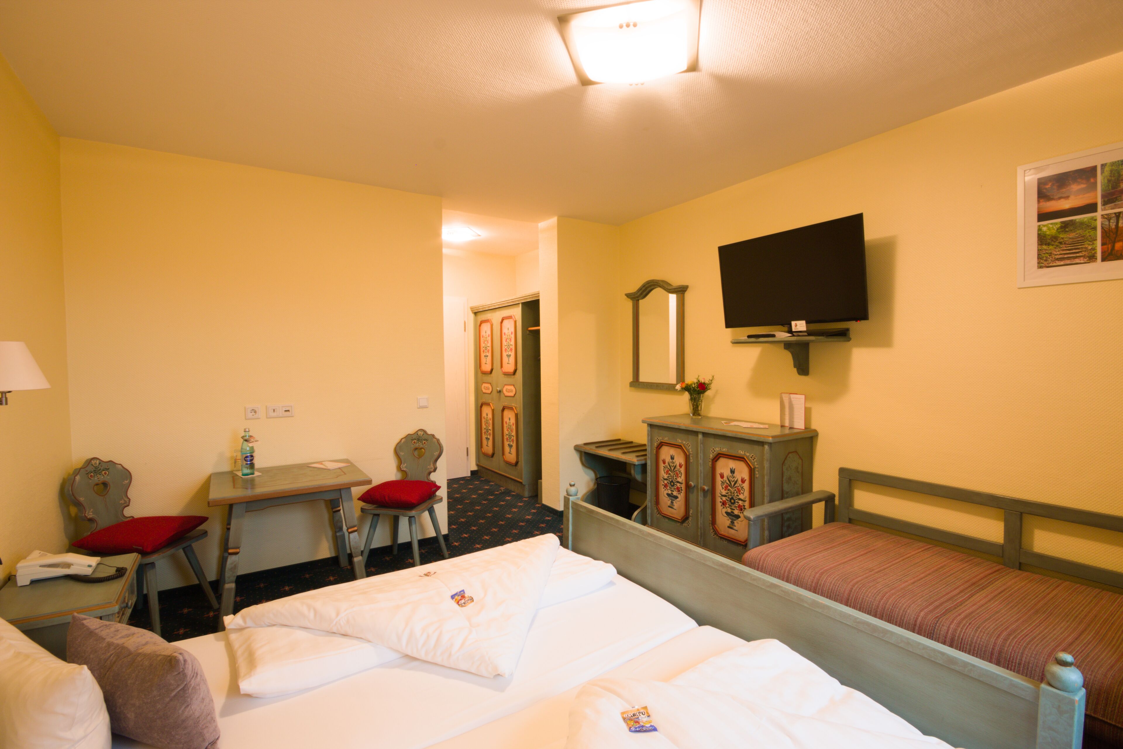 A hotel room with a bed, a desk with a chair, a television, and a wardrobe.