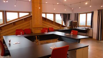 Une salle de conférence avec une longue table, des chaises rouges et un escalier en bois.
