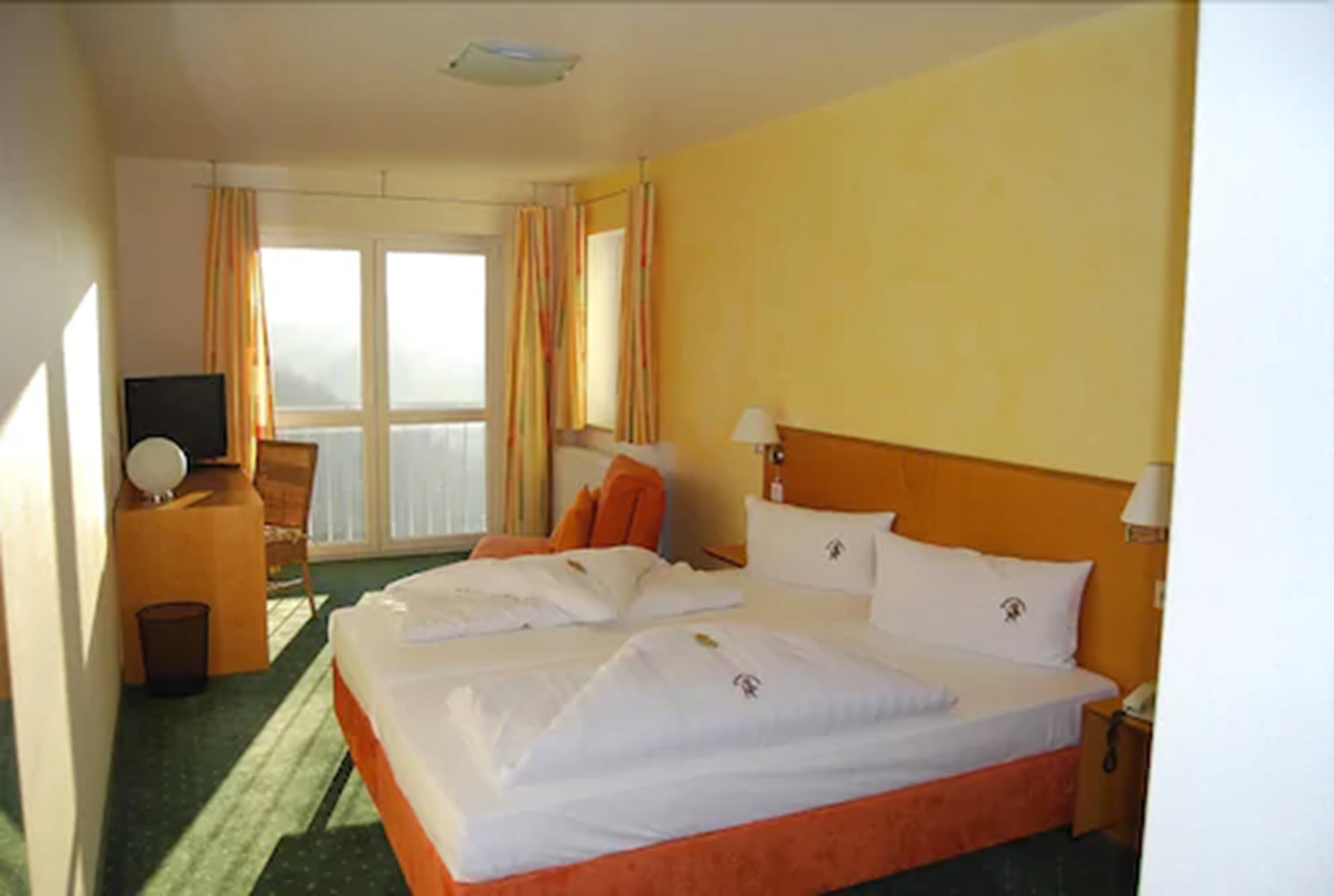 Une chambre d’hôtel avec deux lits, un bureau avec une chaise, une télévision et une fenêtre avec des rideaux.