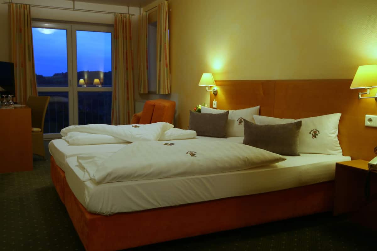 Habitación de hotel con una cama grande, dos lámparas de noche, una silla, un escritorio y una ventana con cortinas.