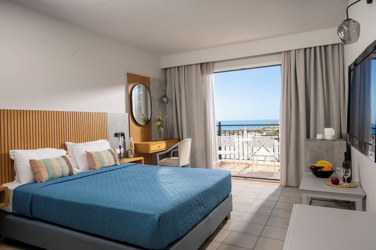 Une chambre d’hôtel comprenant un lit, un bureau, une chaise, une télévision et un balcon avec vue sur la mer.