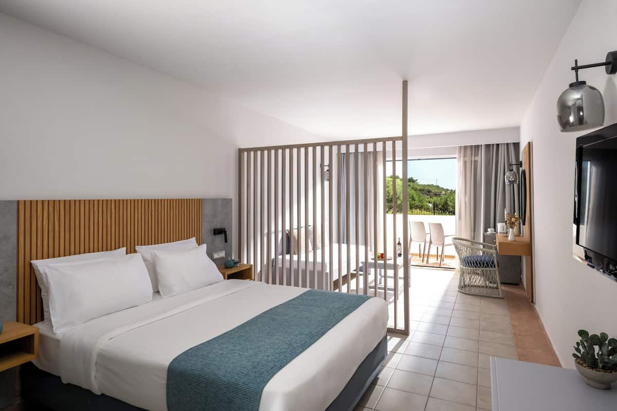Une chambre d’hôtel moderne dotée d’un grand lit, d’un bureau avec un téléviseur à écran plat, d’un coin repas avec des chaises et d’une vue sur l’extérieur.