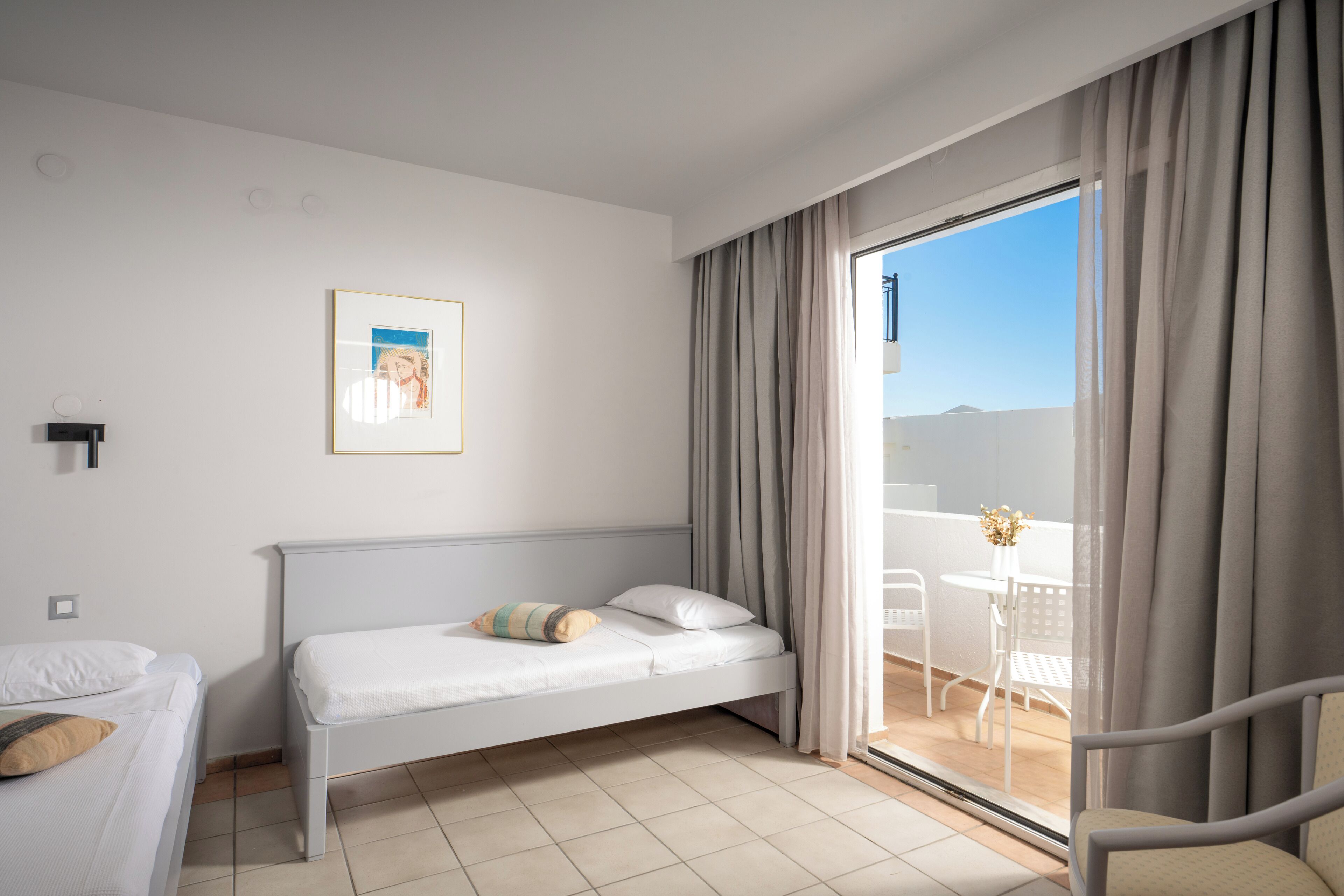 Quarto com cama, uma mesa pequena com cadeiras e varanda com cortinas.