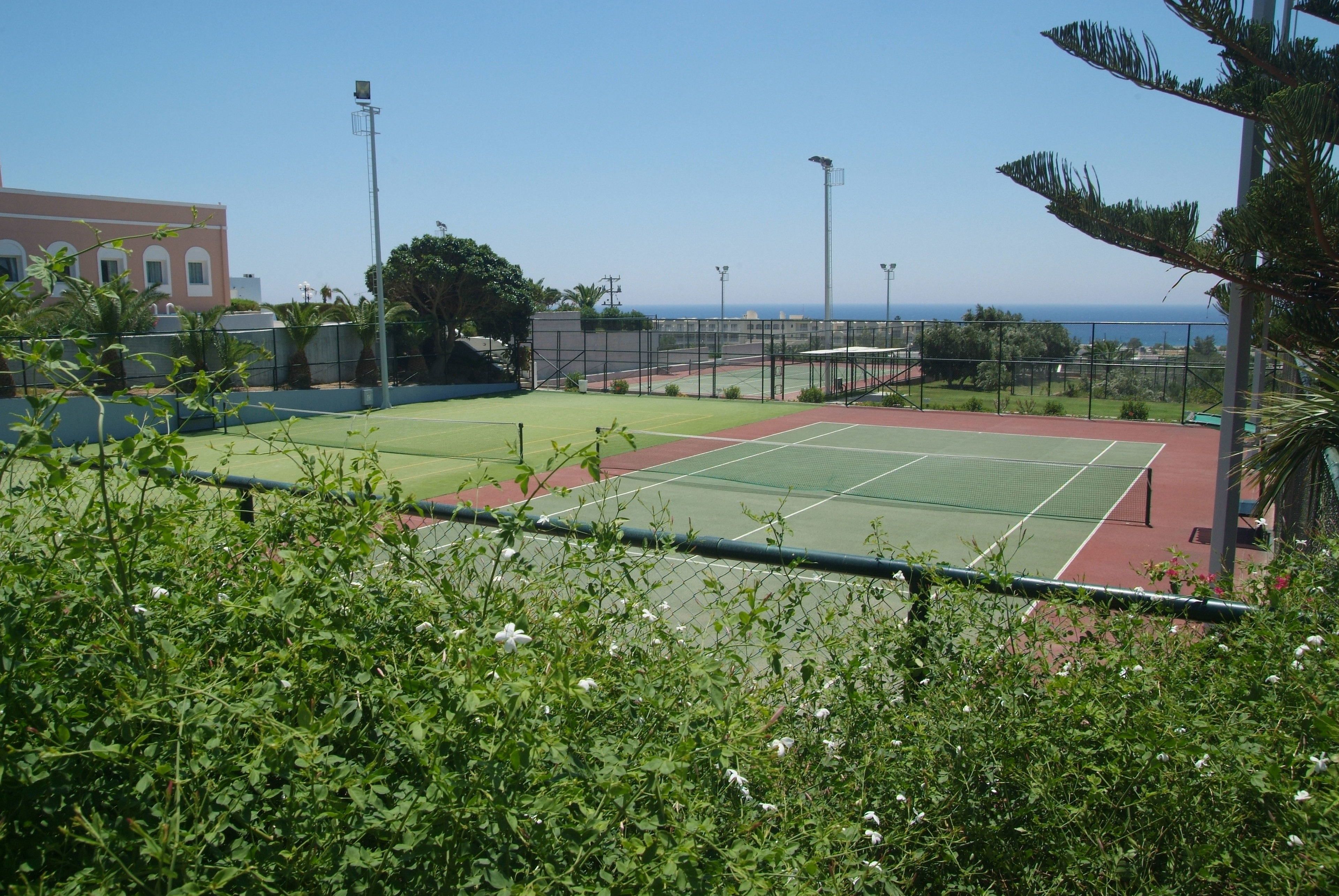 Ein Tennisplatz mit Netz, umgeben von einem Zaun, und ein Gebäude im Hintergrund.