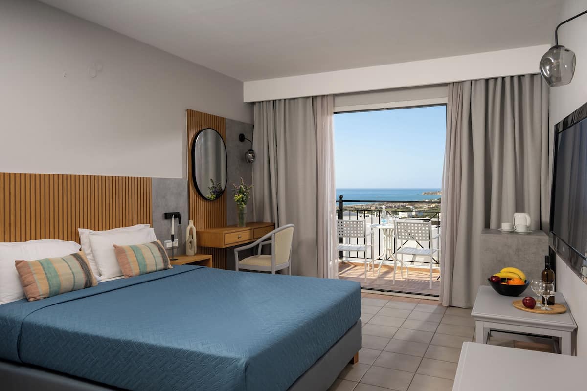 Une chambre d’hôtel équipée d’un lit, d’un bureau, d’une chaise et d’un balcon avec vue sur la mer.