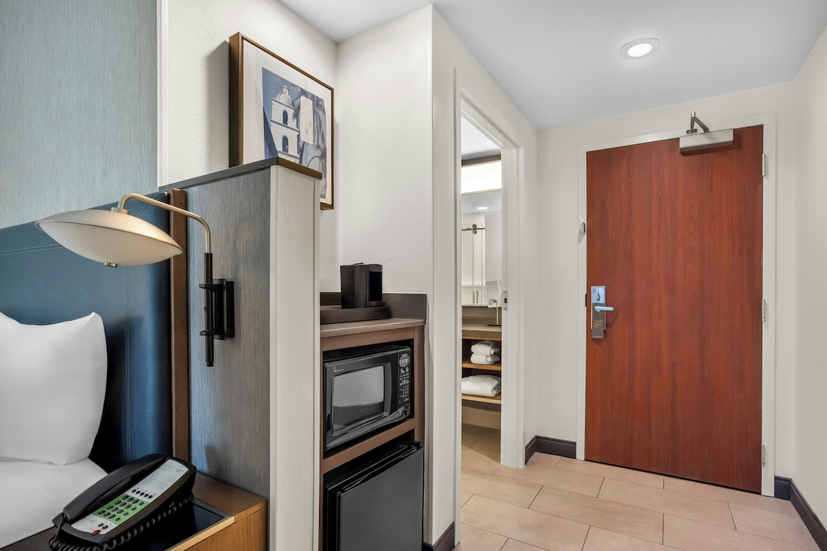 Una habitación de hotel con una cama, un escritorio con teléfono, un microondas y una puerta que da a un baño.