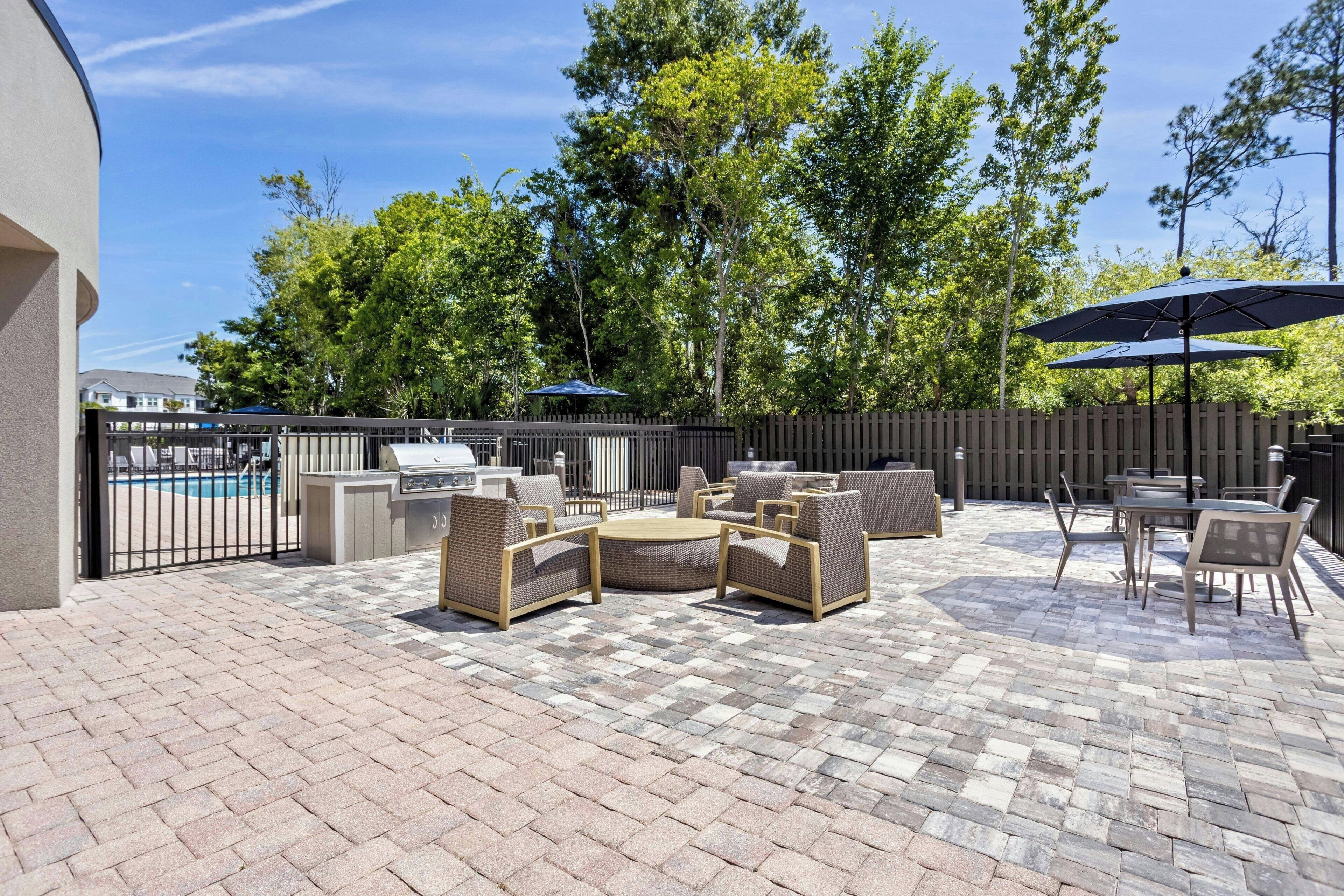 Un patio con mobiliario exterior, una parrilla y una piscina al fondo.