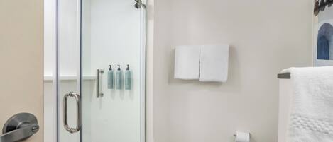 Un baño con cabina de ducha de vidrio, inodoro y perchero con toallas.