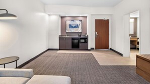 Un hall de hotel con una zona de estar, kitchenette, una puerta y una obra de arte colgada en la pared.