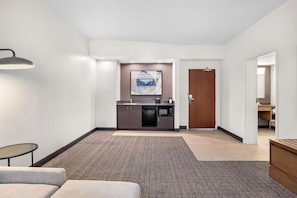 Un hall de hotel con una zona de estar, kitchenette, una puerta y una obra de arte colgada en la pared.