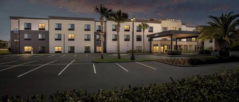 A Courtyard by Marriott hotel with a parking lot and palm trees.