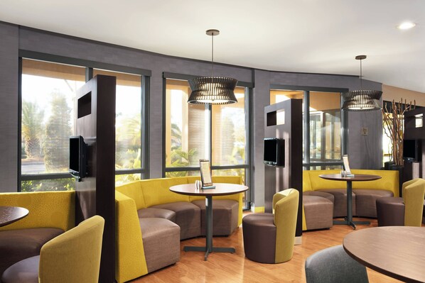 Un interior moderno con asientos amarillos y marrones, ventanas amplias e iluminación colgante.