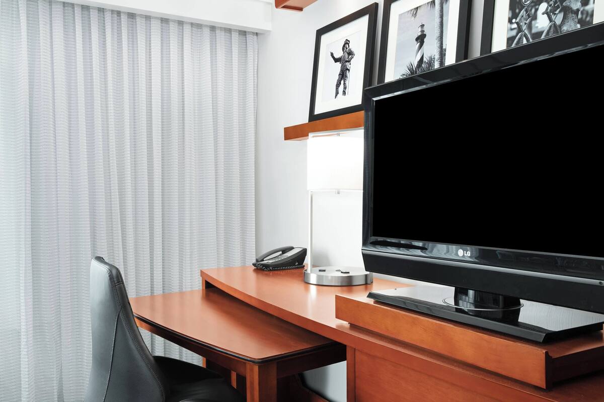 Una habitación de hotel con un escritorio de madera, un televisor de pantalla plana, un teléfono y fotografías enmarcadas en la pared.