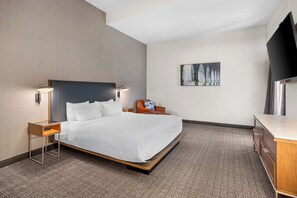 Une chambre d’hôtel avec un lit, des tables de chevet, une télévision, un tableau et un bureau.