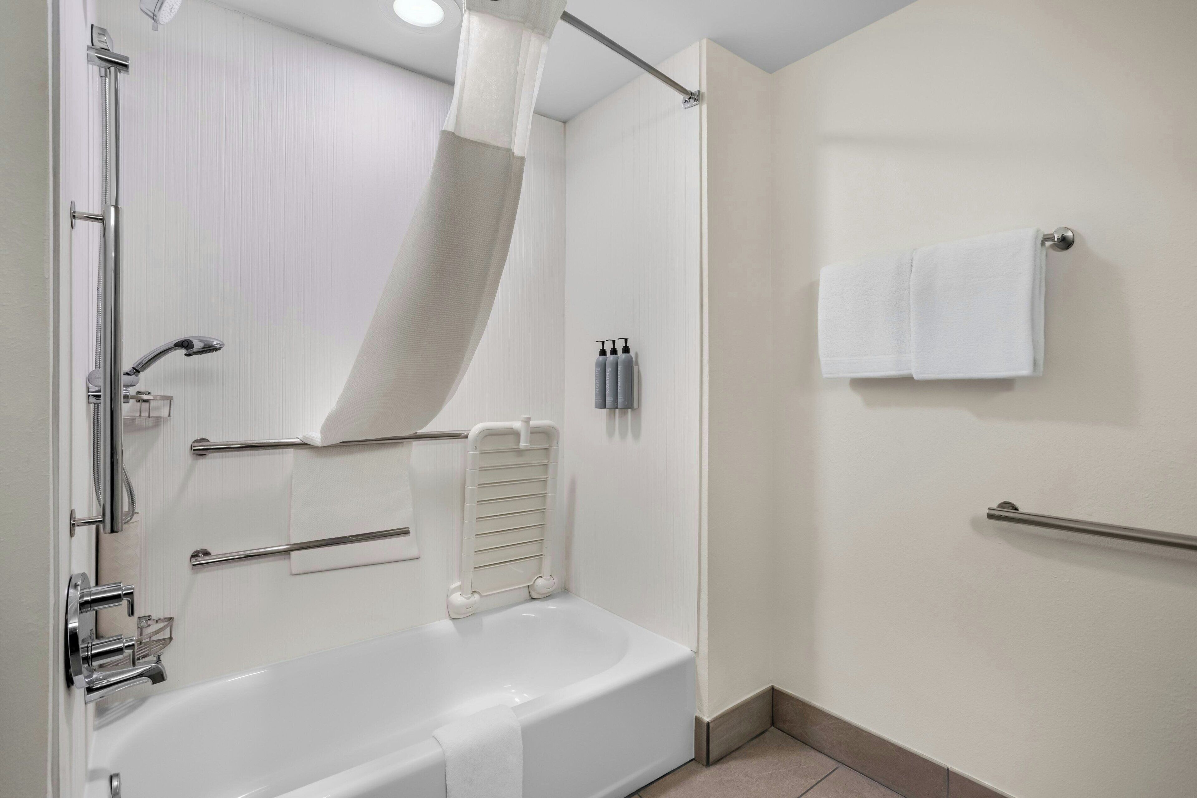 A modern bathroom with a bathtub, shower, and handrails.