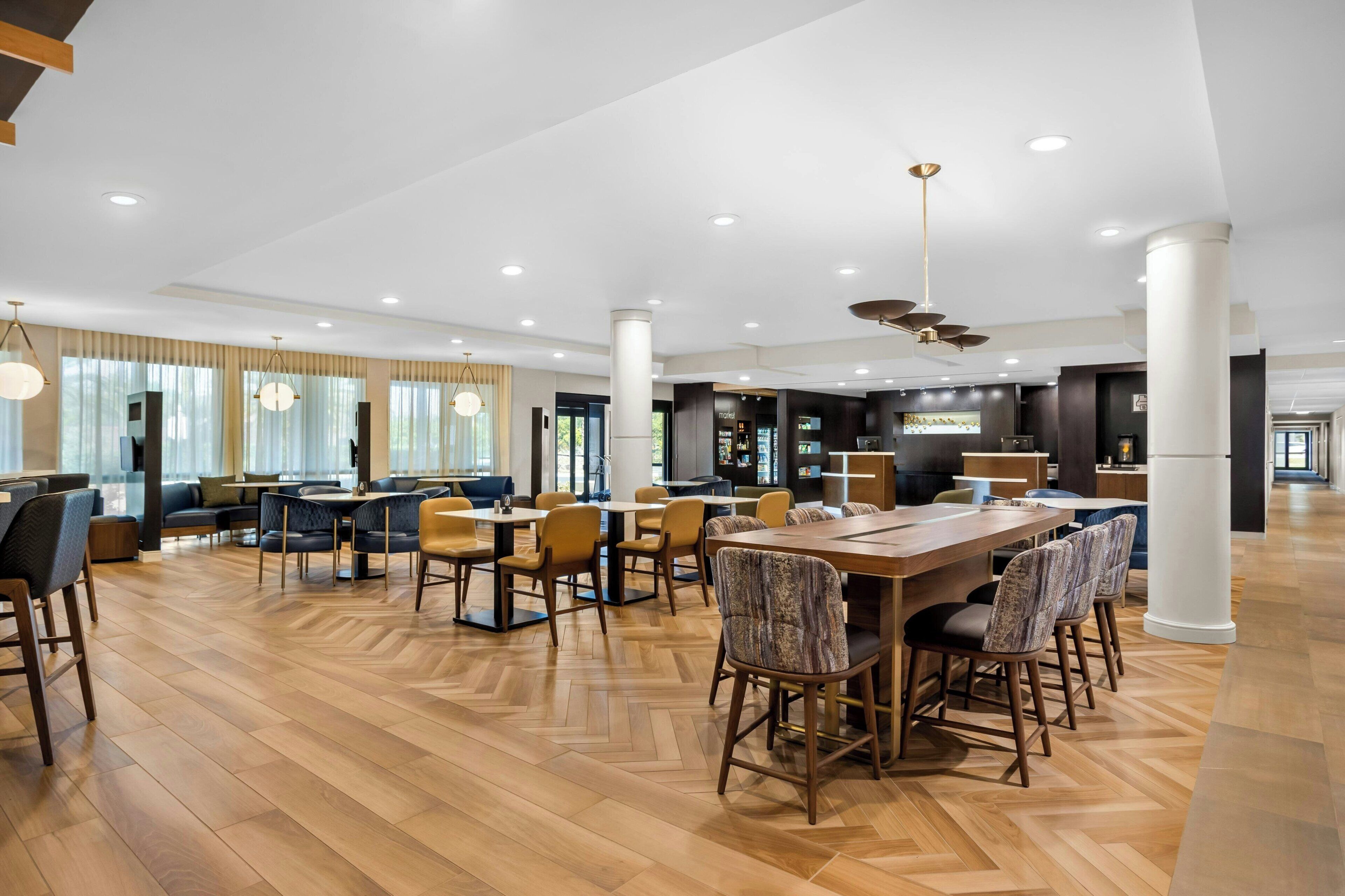 Un amplio vestíbulo de hotel con zona de comedor central, arreglos de asientos y un bar.