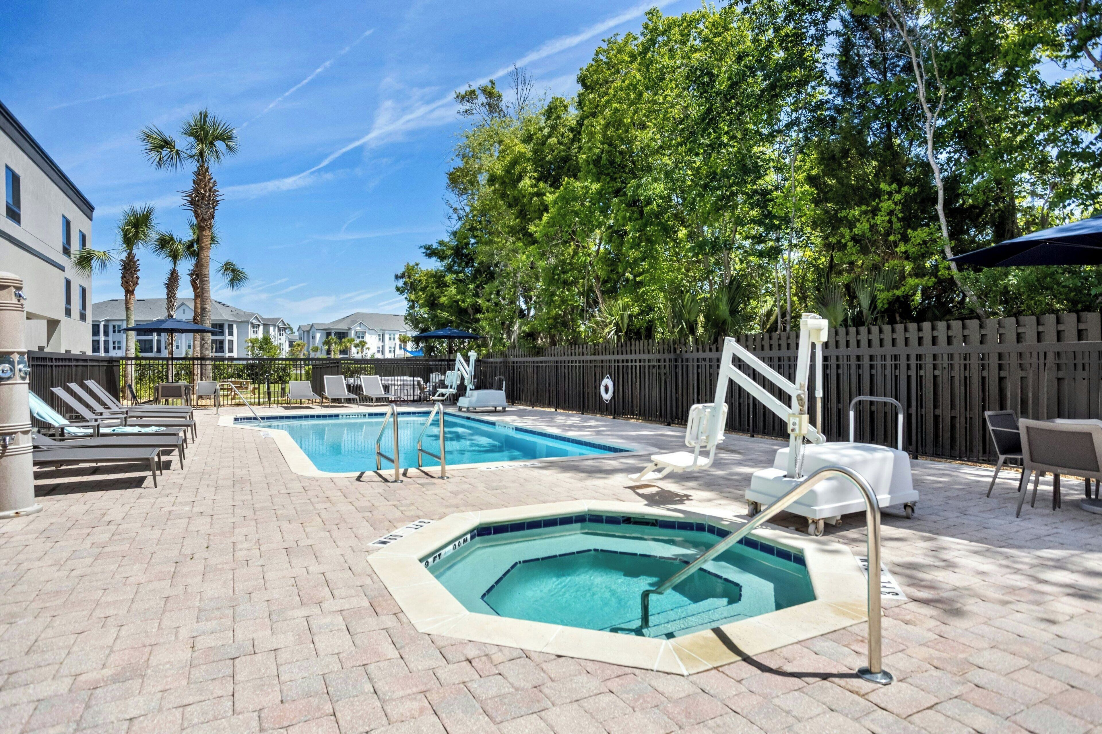 A pool area with two pools, lounge chairs, and a hot tub.