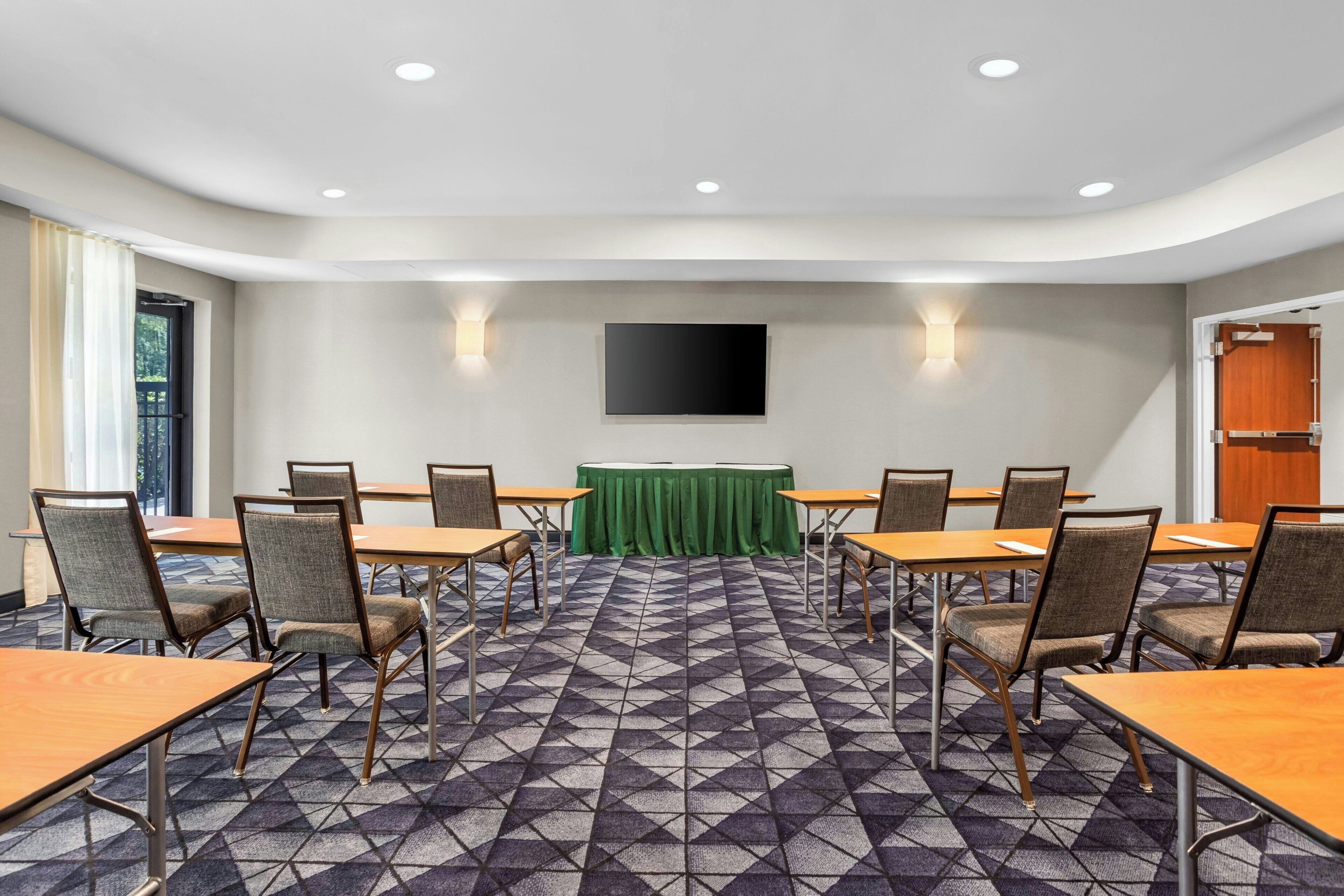 A conference room with a large table, chairs, a green tablecloth, and a flat-screen TV mounted on the wall.