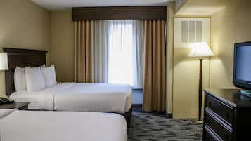 A hotel room with two beds, a television, a lamp, and a window with curtains.