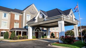 A Country Inn & Suites hotel with a covered entrance, brick facade, and American flag. - Country Inn & Suites by Radisson, Richmond West at I-64, VA (Richmond)