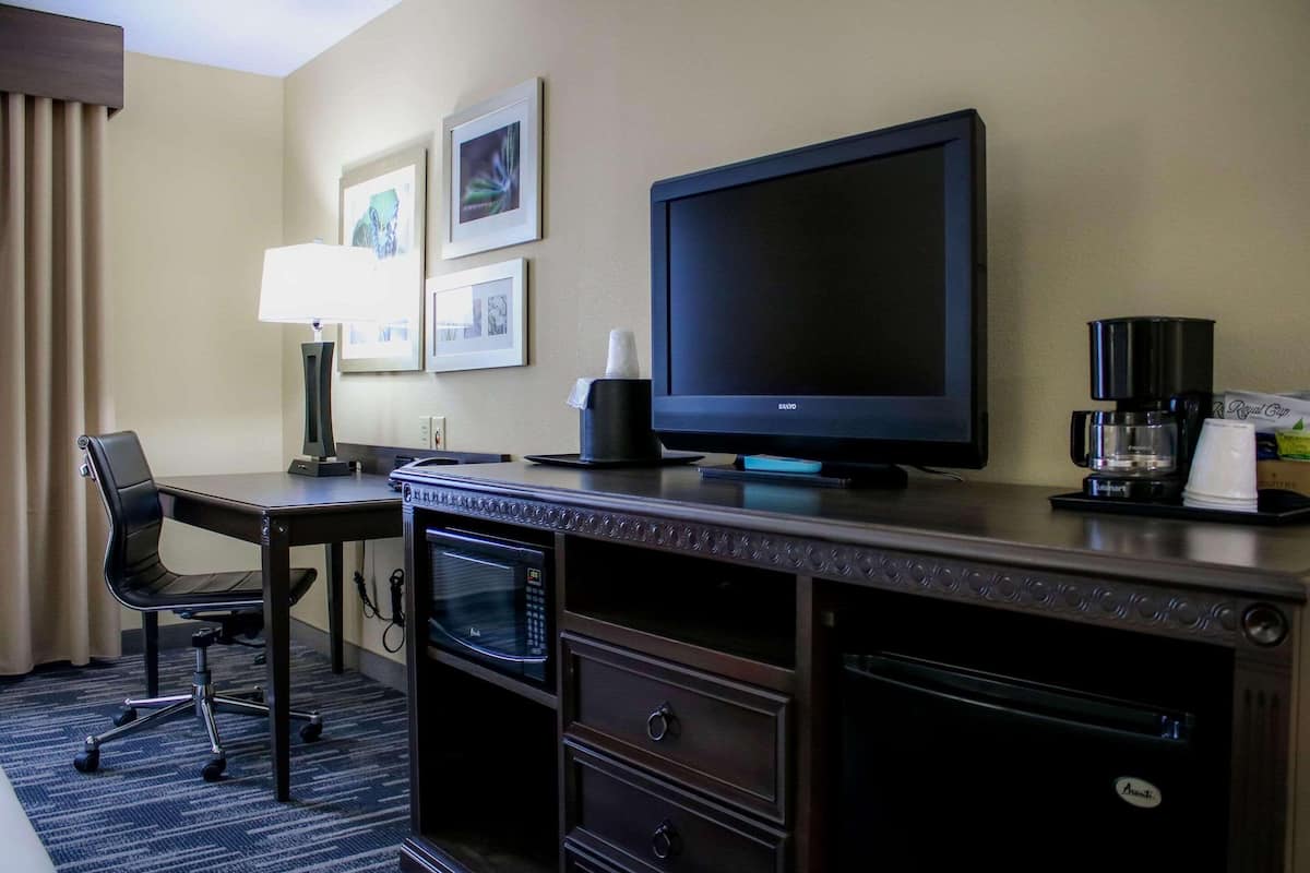A hotel room with a desk, a flat-screen TV, a coffee maker, a microwave, and a chair.