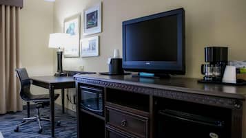 A hotel room with a desk, a flat-screen TV, a coffee maker, a microwave, and a chair.