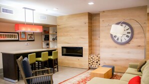 A modern living room with a wooden wall, a television, a sofa, a coffee table, and a dining area with chairs. - Country Inn & Suites by Radisson, Richmond West at I-64, VA (Richmond)