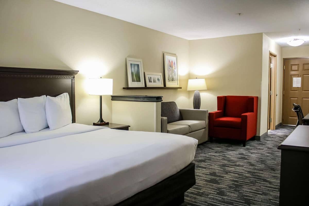 A hotel room with a large bed, a desk, a red chair, and a lamp.