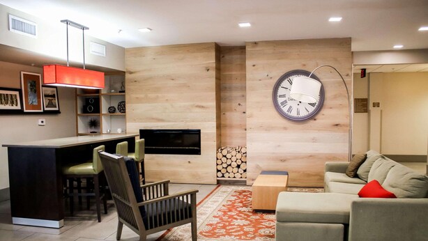 A modern living room with a sofa, a dining area with chairs, a TV, a fireplace, and a clock on the wall. - Country Inn & Suites by Radisson, Richmond West at I-64, VA (Richmond)