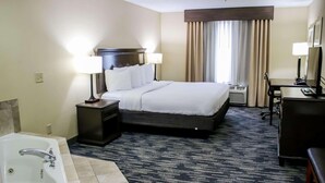 A hotel room with a large bed, a desk, a chair, a desk lamp, a TV, a bathroom with a bathtub, and a window with curtains. - Country Inn & Suites by Radisson, Richmond West at I-64, VA (Richmond)