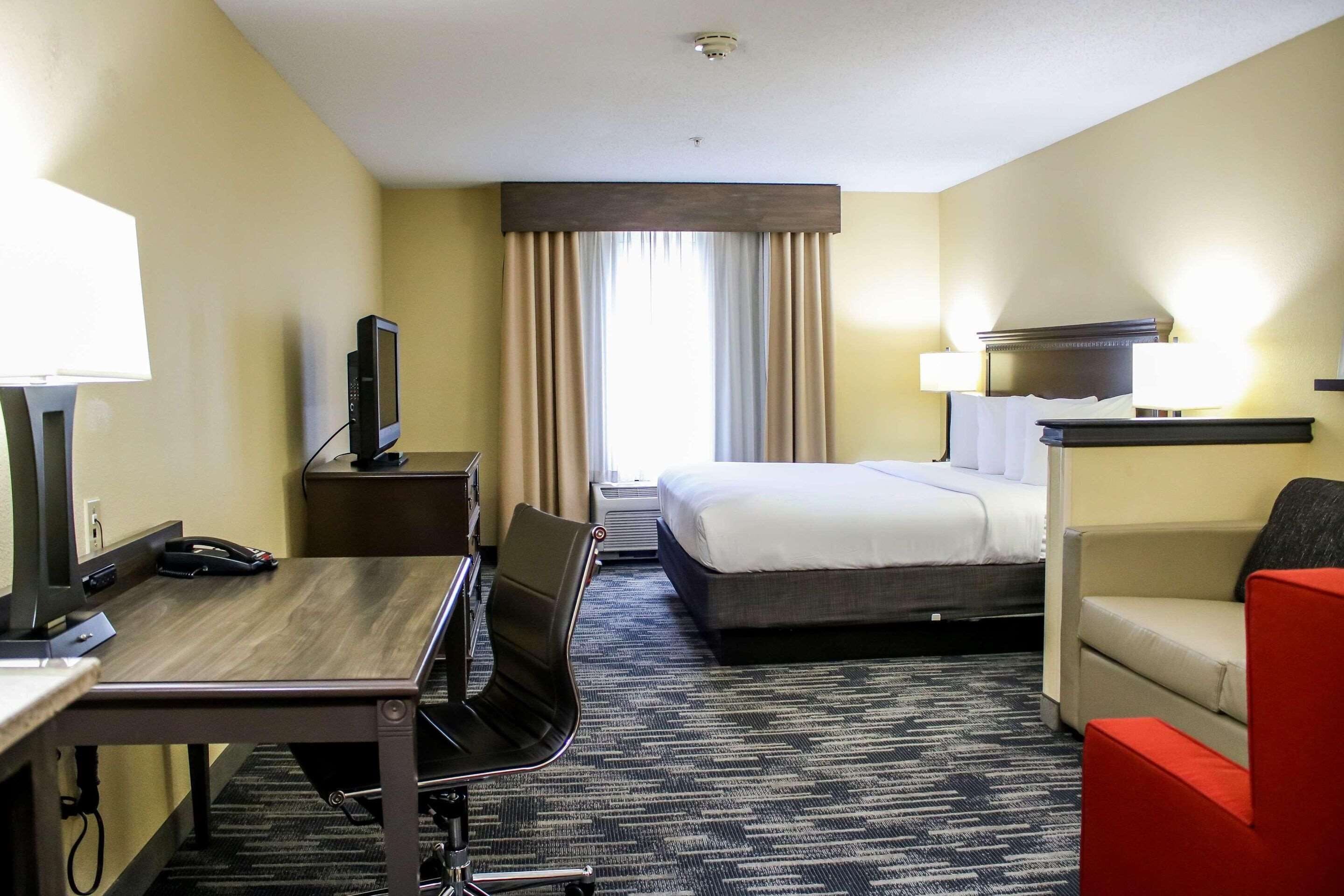 A hotel room with a desk, chair, bed, and a TV.