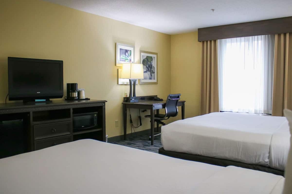 A hotel room with two beds, a desk with a computer, a television, and a coffee maker.