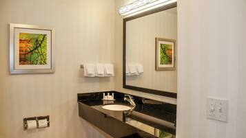 Une salle de bain d’hôtel avec un lavabo à vasque noire, un grand miroir et deux œuvres d’art encadrées accrochées aux murs.