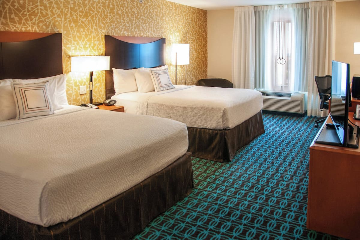 A hotel room with two beds, a desk with a computer, a chair, and a window with curtains.