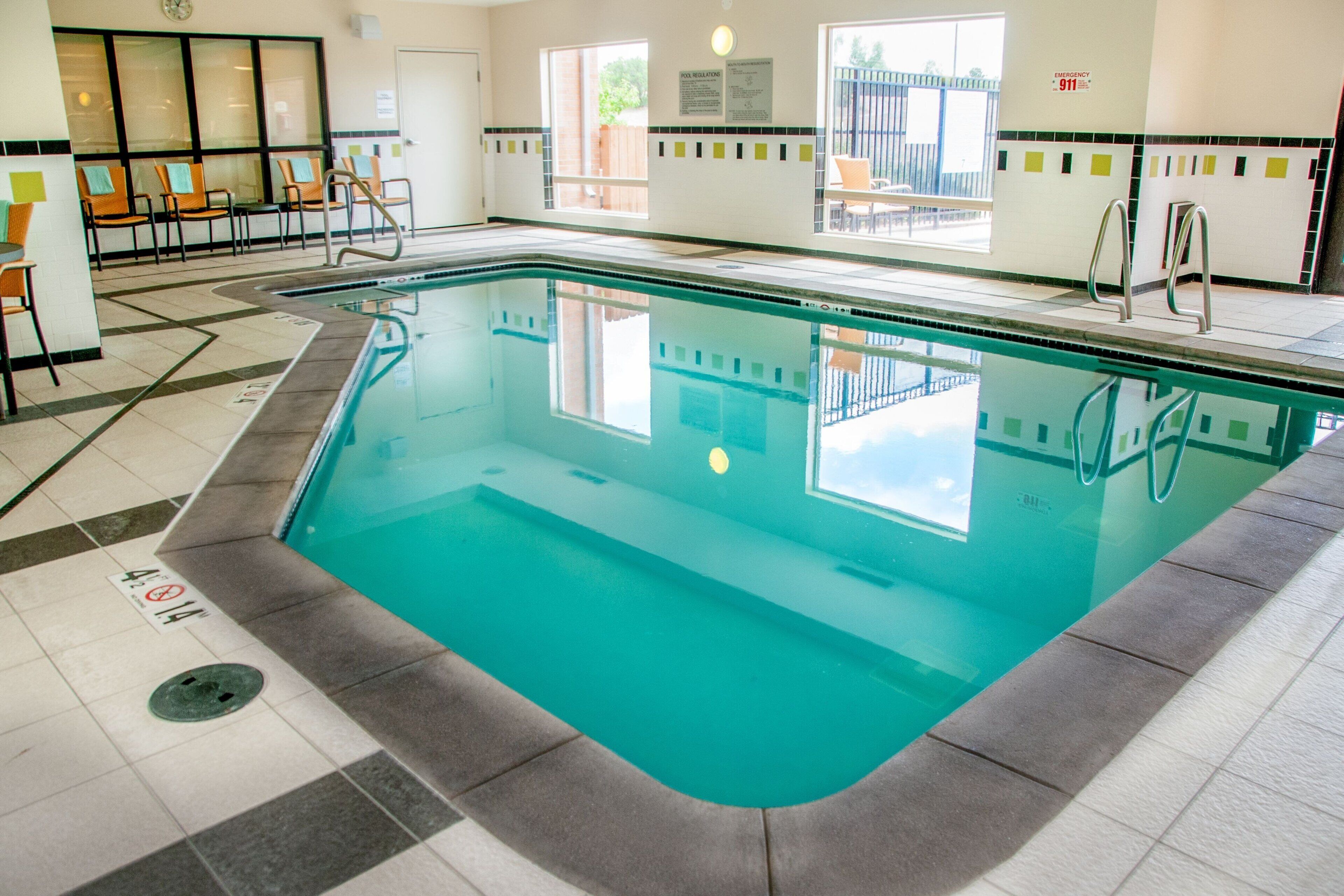 An indoor swimming pool with clear water, a tiled floor, and a view of the outside through large windows.