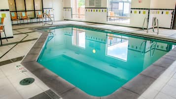 An indoor swimming pool with clear water, a tiled floor, and a view of the outside through large windows.
